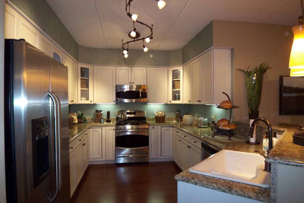 Припотолочная люстра изогнутой вытянутой формы позволяет равномерно осветить все уголки кухонного помещения